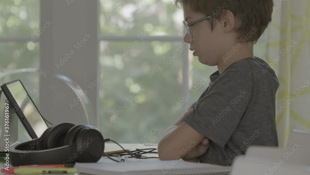 Cute boy in a virtual class at home on a tablet stares out the window Cute boy in a virtual class at home on a tablet stares out the window
