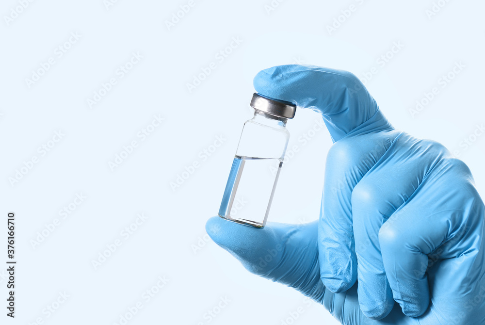 A bottle of vaccine for injection in the doctor's hand on a light blue background A bottle of vaccine for injection in the doctor's hand on a light blue background