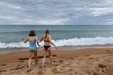 Girls teenagers in swimming suits on a beach of Baikal lake going to water in cloudy weather