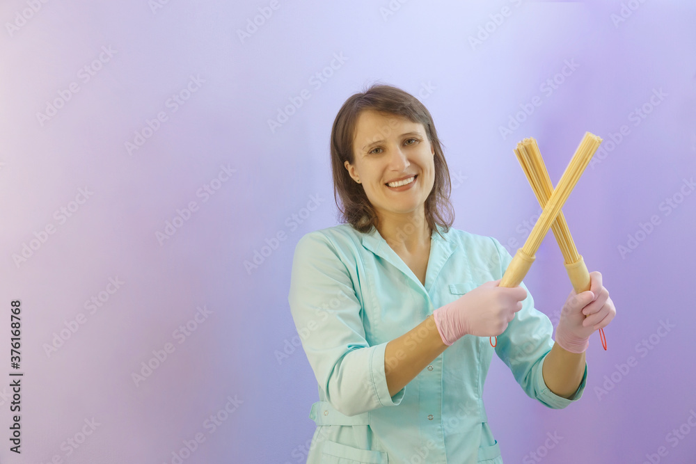Smiling woman masseuse holding massager sticks like a cross in green uniform Smiling woman masseuse holding massager sticks like a cross in green uniform