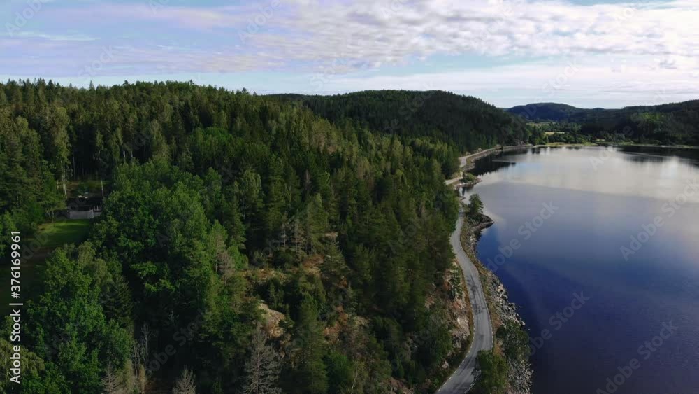 Aerial view of narrow road between calm blue lake and green forest Aerial view of narrow road between calm blue lake and green forest