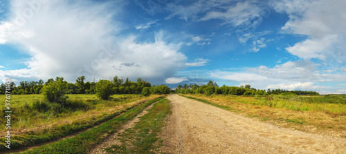 Summer sunny rural landscape with beautiful clouds in blue sky over the country road during sunset photo