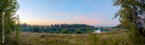 Panoramic view of calm lake and woods at sunrise.
