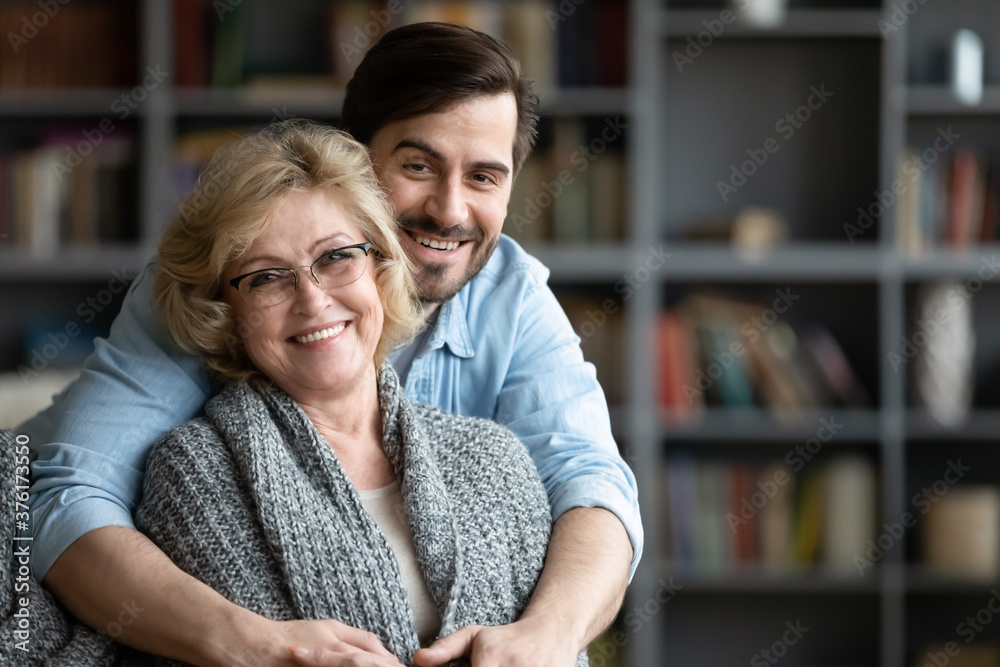 Head shot portrait smiling mature woman and young man hugging, looking at  camera, loving adult son embracing elderly mother from back, standing in  modern living room together, posing for photo Stock Photo