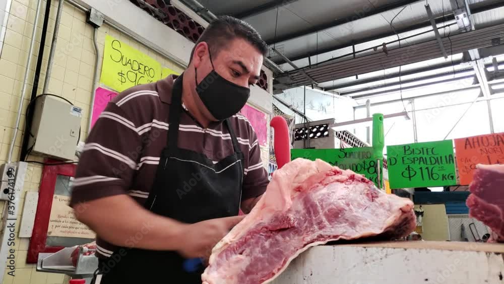 Carnicero con cubrebocas cortando la carne en el mercado 
