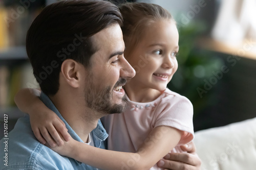 Close up dreamy young father and little daughter hugging, looking to aside, dreaming about good future, planning, sitting on cozy sofa in living room together, family enjoying leisure time at home © fizkes
