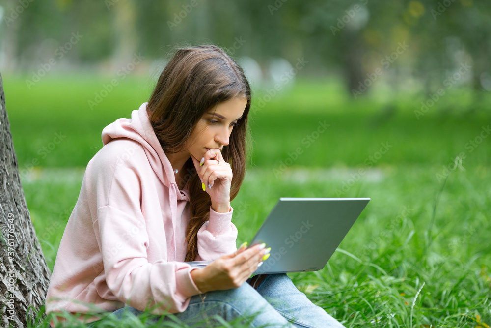 Pensive young woman having a working with laptop, while sitting on the grass in campus park. Pensive young woman having a working with laptop, while sitting on the grass in campus park.
