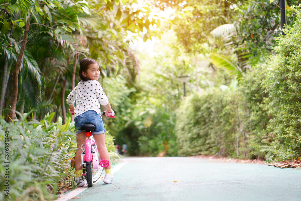 Asian child or kid girl smile and biker to cycling fun on bike or people riding bicycles on public park or garden and green tree with road of bicycle for sport exercise to healthy on family holiday Asian child or kid girl smile and biker to cycling fun on bike or people riding bicycles on public park or garden and green tree with road of bicycle for sport exercise to healthy on family holiday
