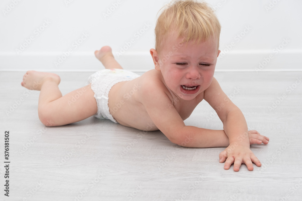 baby blonde boy crying lying on the field.