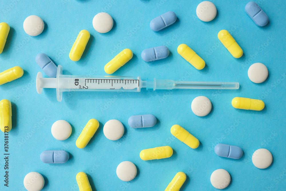 Various pills and syringe on a blue background. Various pills and syringe on a blue background.