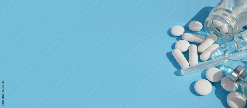 white pills are sprinkled on a blue background. in a transparent jar white pills near ampoules. banner with place for text in the middle and on the left. view from above