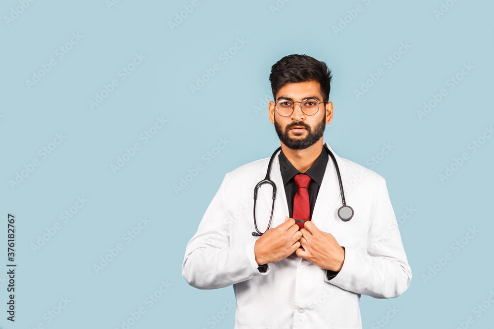 Cute Indian / Asian doctor wearing glasses with stethoscope, tie and white coat on light blue background. Cute Indian / Asian doctor wearing glasses with stethoscope, tie and white coat on light blue background.