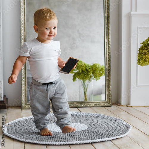 Little child boy plaing with phone on knitted carpeet on the wooden floor indoor. Knitted style in the interior. Warm and cozy. Playful children photo