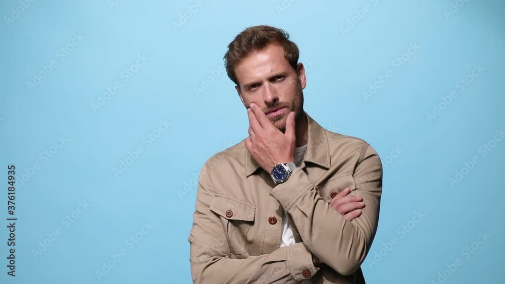 young casual guy with attitude crossing his arms, touching his face, turning ro a side and posing sensually on blue background young casual guy with attitude crossing his arms, touching his face, turning ro a side and posing sensually on blue background