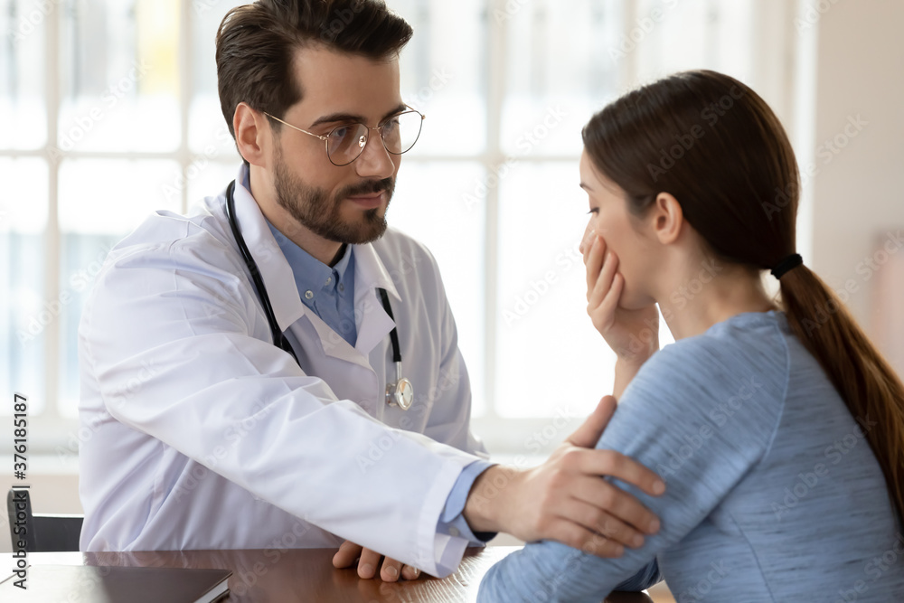 Close up caring doctor therapist wearing white uniform with stethoscope touching frustrated patient shoulder, physician gp comforting upset unhealthy young woman at medical appointment Close up caring doctor therapist wearing white uniform with stethoscope touching frustrated patient shoulder, physician gp comforting upset unhealthy young woman at medical appointment