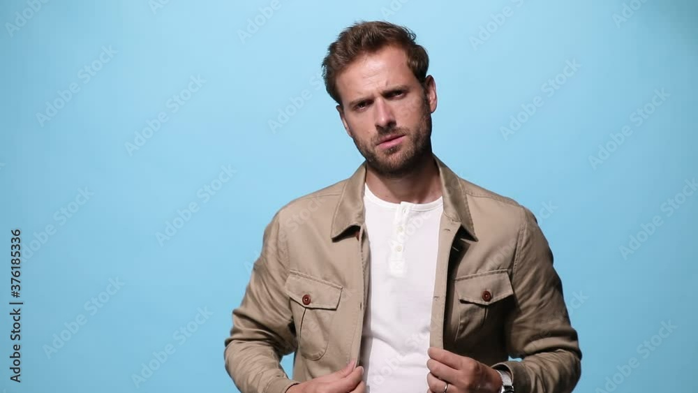 cool fashion man adjusting his jacket with attitude, looking at the camera and posing on blue background cool fashion man adjusting his jacket with attitude, looking at the camera and posing on blue background
