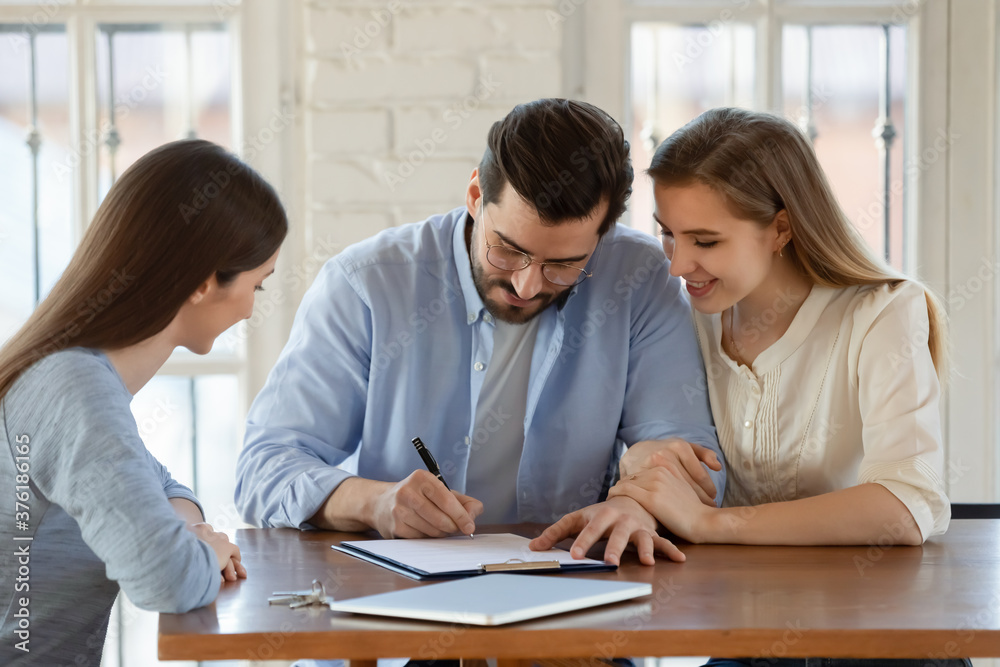Happy young married couple signing contract, making successful deal with lawyer, realtor or financial advisor, smiling young man and woman holding hands, purchasing real estate, first house Happy young married couple signing contract, making successful deal with lawyer, realtor or financial advisor, smiling young man and woman holding hands, purchasing real estate, first house