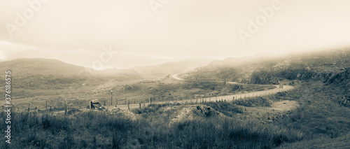 Monochrome image of the misty hills of Molls Gap in Kerry, Ireland. The narrow windy road disappears in to the fog. photo