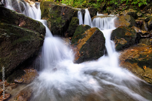 Mountain waterfall flows among green forest and runs down the beautiful gray stones. Amazing summertime wallpaper background.