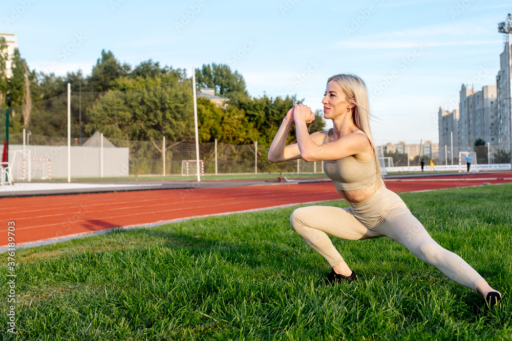 Fototapeta premium Beautiful young blonde doing lunges exercises during training in the stadium