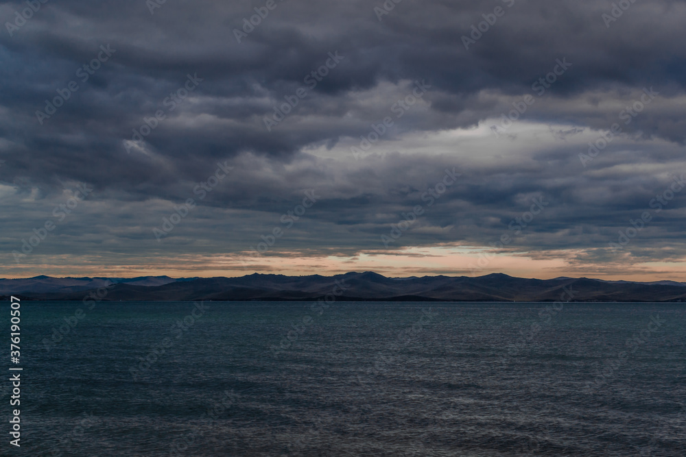 view of the clear calm undulating blue water of Lake Baikal, mountains on the horizon, sunset clouds