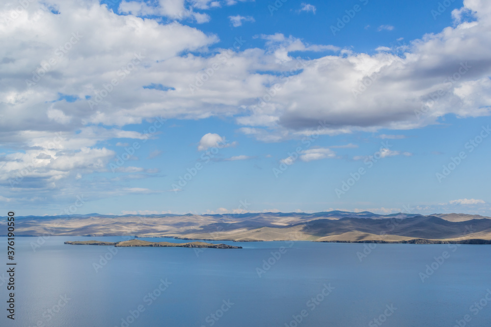 view of the clear calm undulating blue water of Lake Baikal, mountains on the horizon, white clouds, blue sky