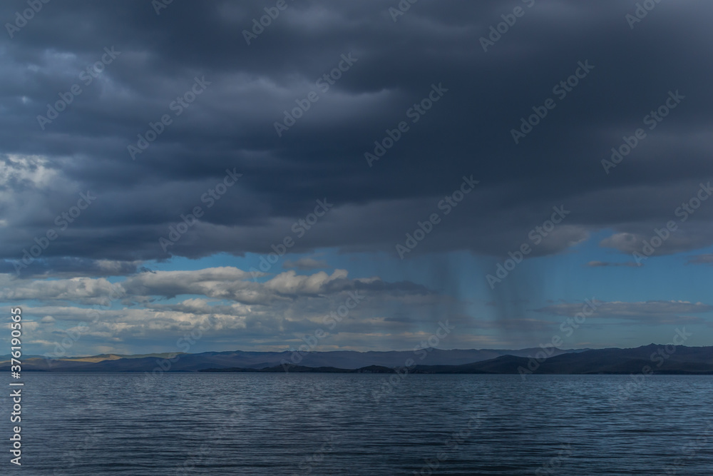 view of the clear calm undulating blue water of Lake Baikal, mountains on the horizon, rain clouds, shower