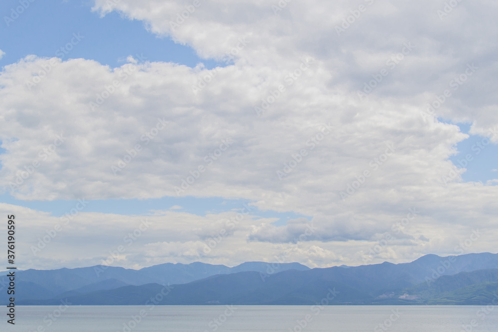 view of the clear calm undulating  water of Lake Baikal, blue mountains on the horizon, white soft clouds background