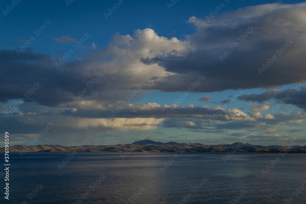 view of the clear calm undulating blue water of Lake Baikal, mountains on the horizon, sunset clouds background