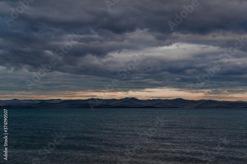 view of the clear calm undulating blue water of Lake Baikal, mountains on the horizon, sunset clouds © SymbiosisArtmedia