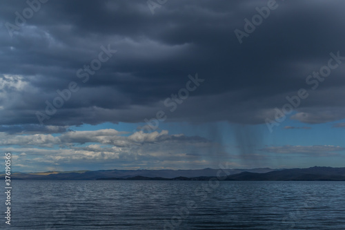 view of the clear calm undulating blue water of Lake Baikal  mountains on the horizon  rain clouds  shower