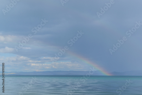 view of the clear calm undulating blue water of Lake Baikal  mountains on the horizon  colorful rainbow after rain