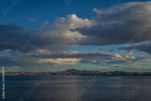 view of the clear calm undulating blue water of Lake Baikal, mountains on the horizon, sunset clouds background © SymbiosisArtmedia