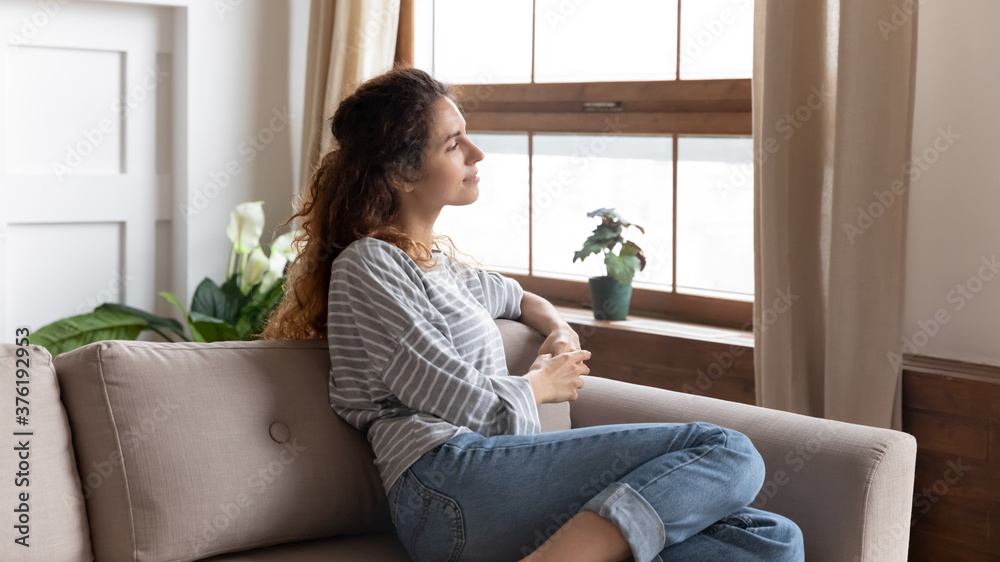 Thoughtful relaxed woman in casual clothes rest on couch in cozy modern living room looks out the window enjoy city admires view, daydreaming, smiling lost on pleasant thoughts spend weekend at home Thoughtful relaxed woman in casual clothes rest on couch in cozy modern living room looks out the window enjoy city admires view, daydreaming, smiling lost on pleasant thoughts spend weekend at home
