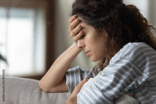 Close up woman closed eyes cover face with palm sit on sofa hug cushion feel despair, infertility as result of abortion, health problem, suffer from headache chronic migraine, break up divorce concept