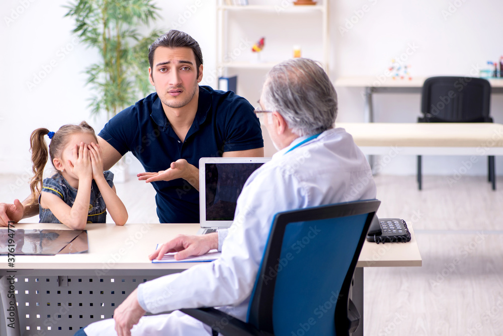 Fototapeta premium Young father and his daughter visiting old male doctor