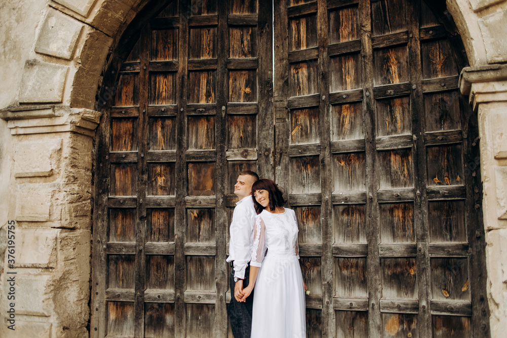 Beautiful couple leaning their backs to each other on the background of a huge old gate.