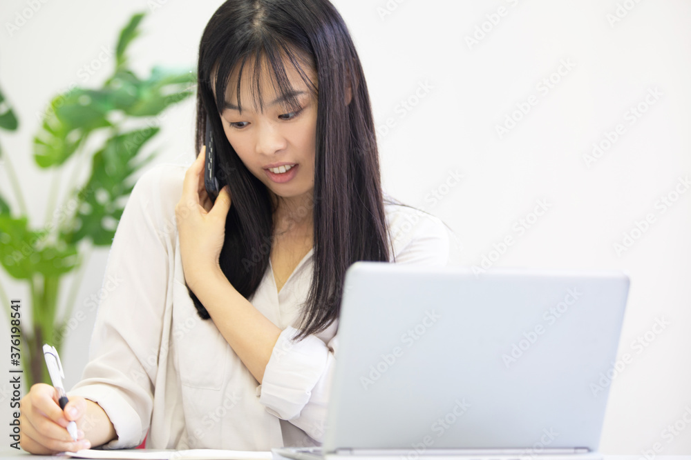 オフィスで電話をかけながらメモをとる女性 オフィスで電話をかけながらメモをとる女性