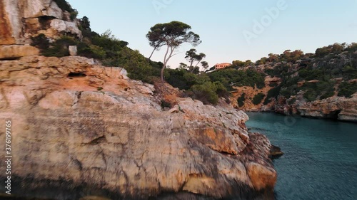 Aerial flying among trees and revealing the rugged coastline of Mallorca and Cala s'Almunia at sunset photo