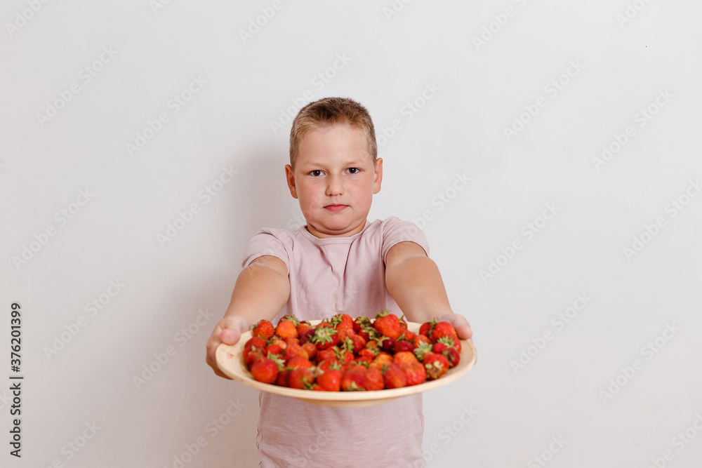Serious full eight-year-old boy holds a plate of ripe strawberries Serious full eight-year-old boy holds a plate of ripe strawberries