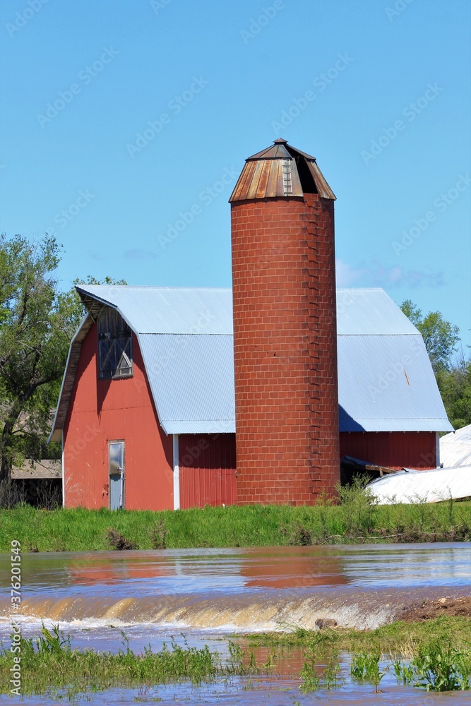 red barn and silo with blue sky and flood water north of Hutchinson Kansas USA out in the country.