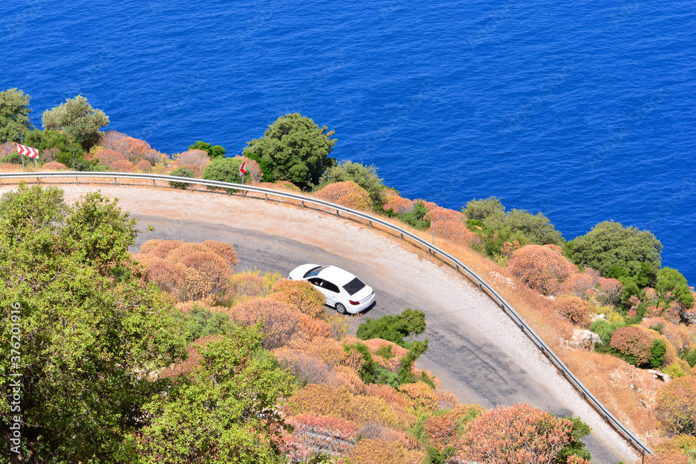 Fototapeta premium Car rental during the travel concept. White car driving by the serpentine road over the sea. Beautiful mediterranean landscape.