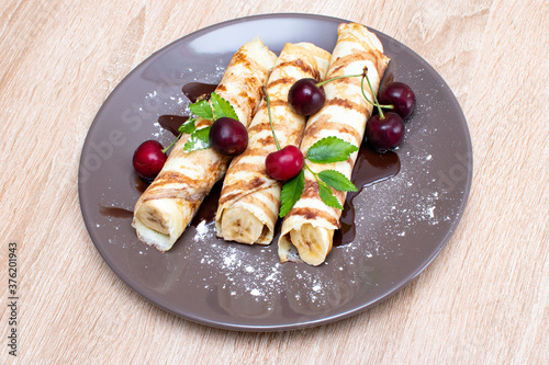 Pancakes with banana and strawberries on a plate. Banana wrapped in a pancake and with strawberries on top. Breakfast with Pancakes with berries and banana and chocolate..