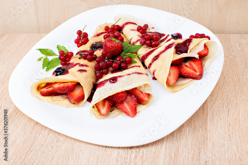 Pancakes with cranberries and strawberries on a plate. Pancakes with berries, strawberries and chocolate syrup. Breakfast with pancakes with strawberries and berries on a plate..