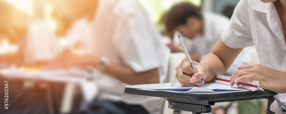Exam at school with student's taking educational admission test in class, thinking hard, writing answer in university classroom, education and world literacy day concept
