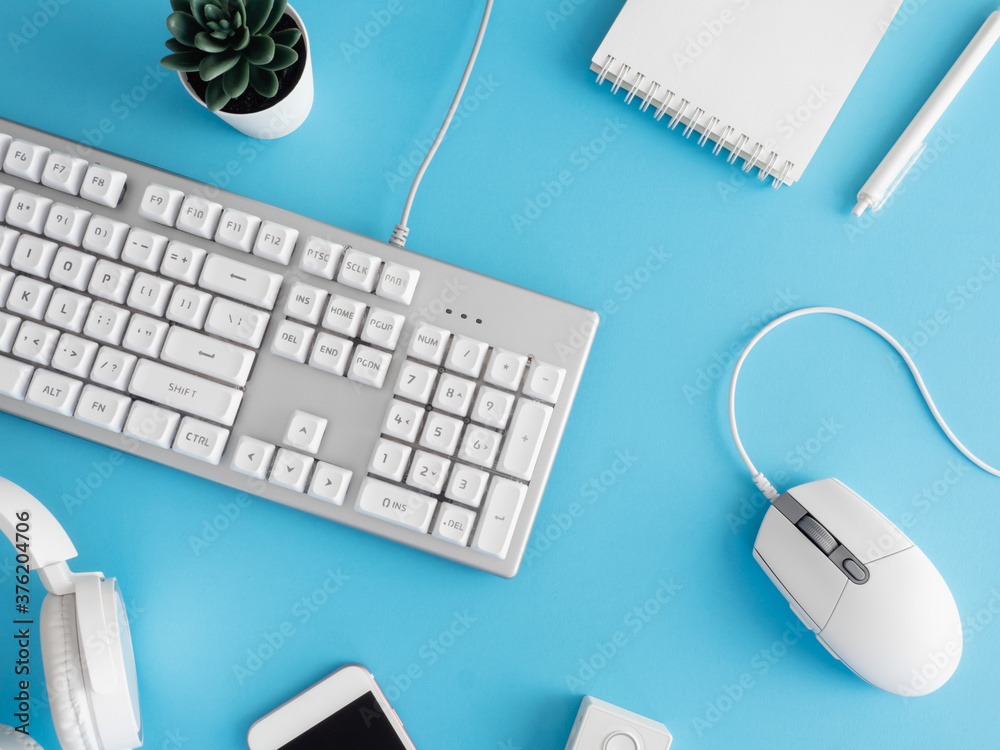 top view of office desk table with notebook, plastic plant, smartphone and keyboard on blue table background, graphic designer.