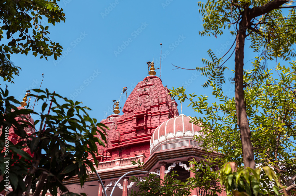 Exterior view of the famous red Digambar jain temple through green tree leaves and blue sky background. A famous Indian religious place.