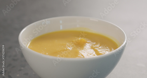 Pumpkin cream soup in a white bowl on concrete backdrop