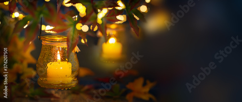 Festive autumn lighting decor. Candle in a jar with rain drop, hanging on tre...