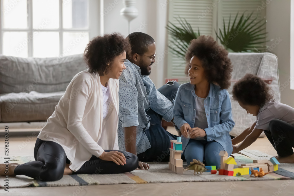 Loving young african ethnicity couple parents sitting on floor carpet, enjoying playing toys with cheerful funny mixed race kids sibling at home. Happy multiracial bonding family involved in game. Loving young african ethnicity couple parents sitting on floor carpet, enjoying playing toys with cheerful funny mixed race kids sibling at home. Happy multiracial bonding family involved in game.